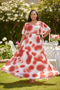Red tie-dye spot print off-shoulder maxi dress styled with gold sandals in garden setting